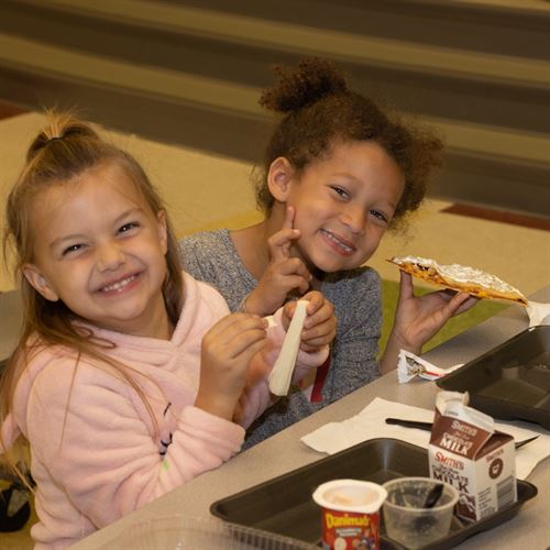 girl in pink sweater and girl in gray sweater eating lunch in cafeteria